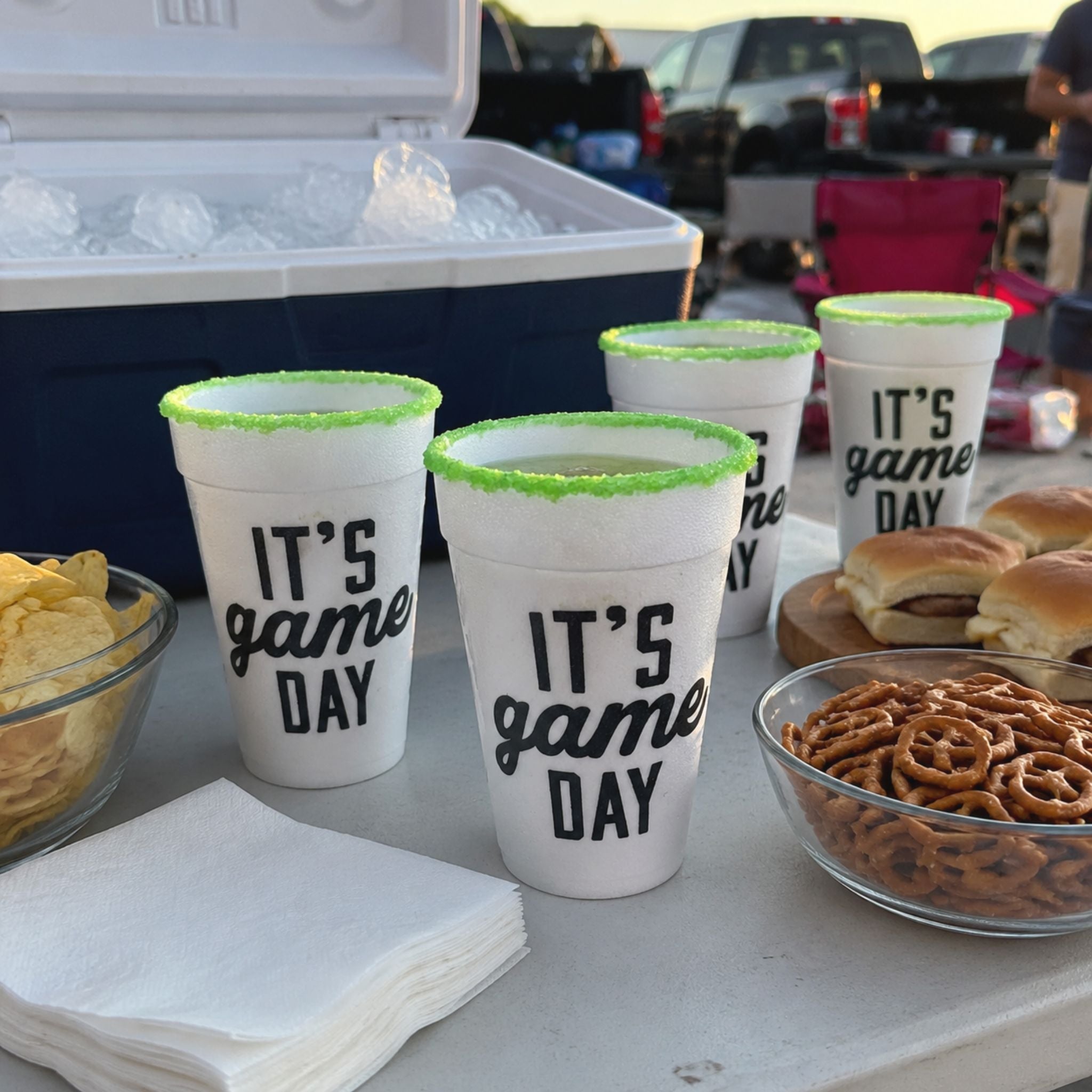Rita Rims Game Day Salt & Lime cups beside a packed cooler, ice, napkins, and simple tailgate snacks.