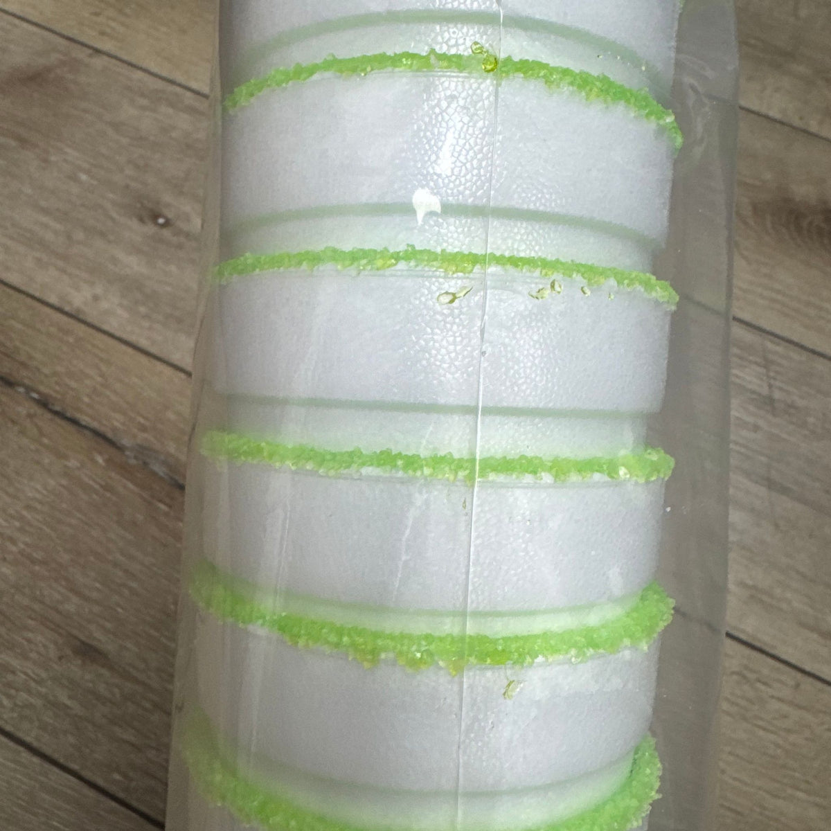 A clear plastic-wrapped foam roll with multiple horizontal white foam bands separated by bright green textured lines, photographed on a wood floor.