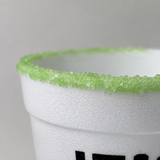 A close-up of a white textured cup rimmed with bright green sugar crystals, with part of a black printed logo visible on the side.