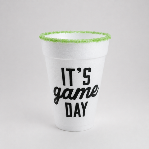 A white foam cup with 'IT'S game DAY' printed in black on the front, featuring a bright green sugar-rimmed edge, set against a neutral light gray background.