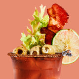Bloody mary cocktail with bacon, lime, and olives on a pink background