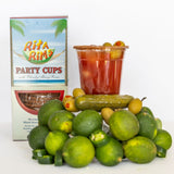 Rita Rims party cups with Bloody Mary mix, limes, and pickles on a white background