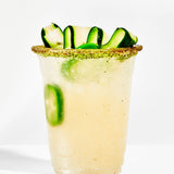 Cocktail with cucumber slices and a green rim on a white background