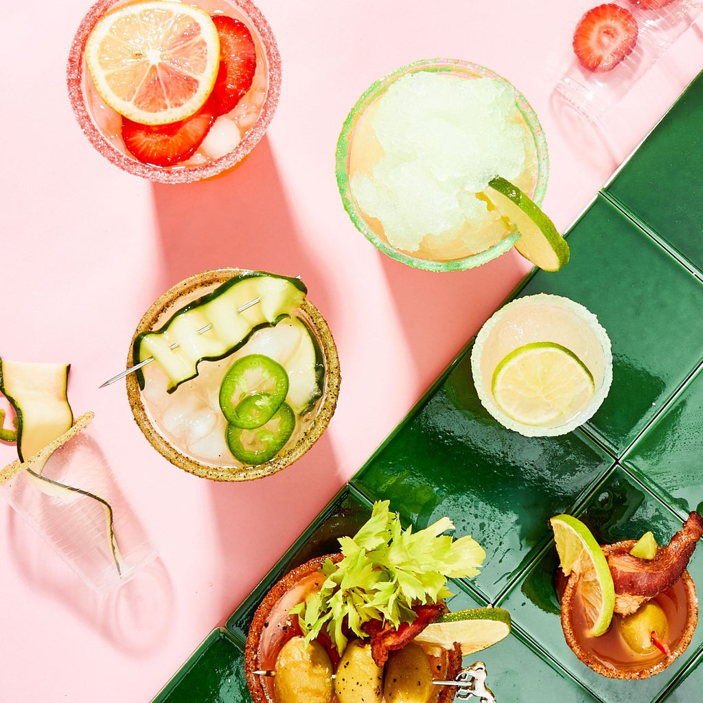 Assorted small appetizers on a green tray with a pink background