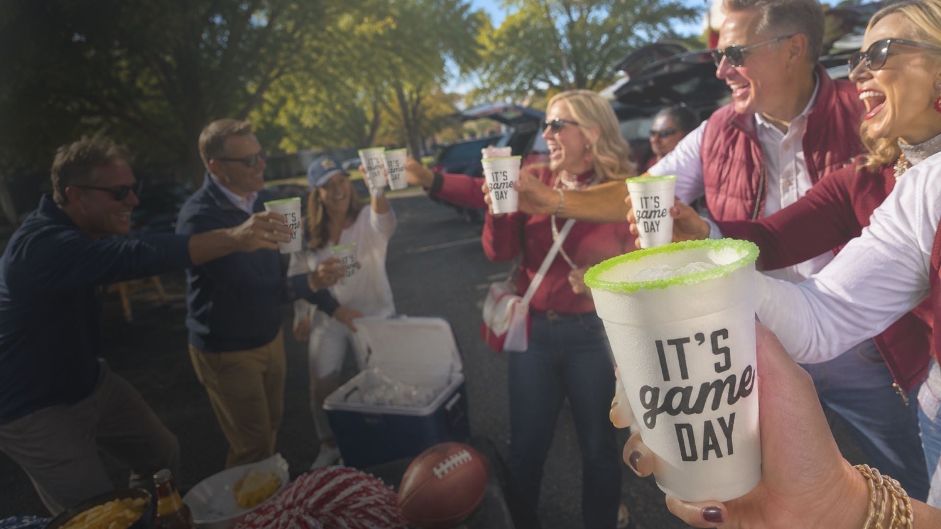 A group of people outdoors at what looks like a game or event, holding white paper cups with black text reading 'IT'S game DAY' and bright green Salt & Lime Rims. One person in the foreground holds a cup close to the camera.