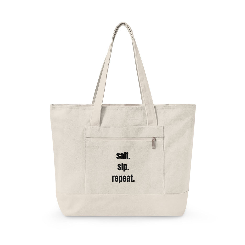 An off-white canvas tote bag with black text reading 'salt. sip. repeat.'