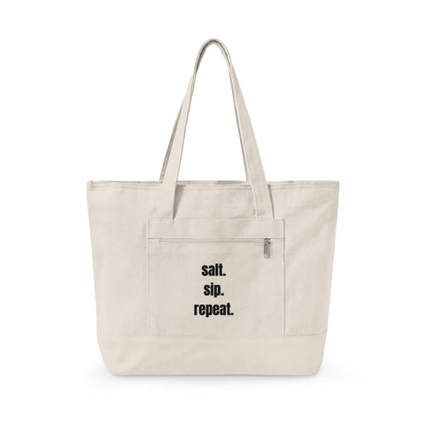 An off-white canvas tote bag with black text reading 'salt. sip. repeat.'