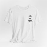 A white short-sleeve crewneck t-shirt with the text 'salt. sip.repeat'