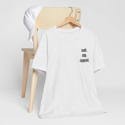 A light heather gray t-shirt with black text reading 'salt. sip. repeat'